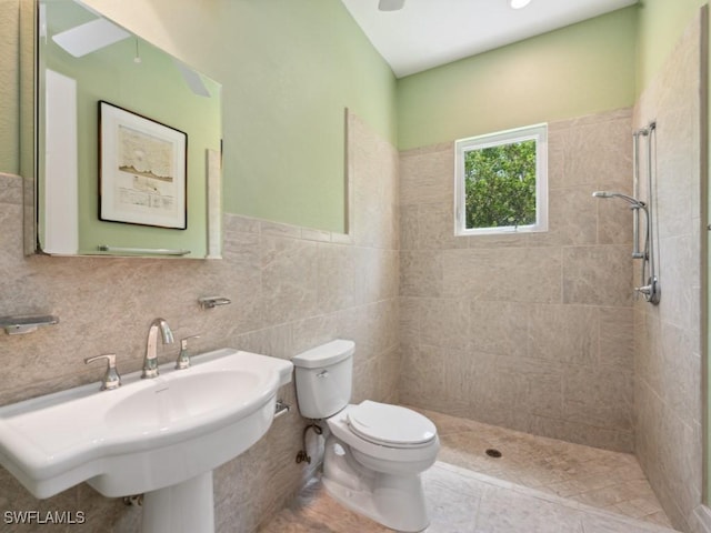 bathroom featuring tiled shower, a sink, tile walls, and toilet