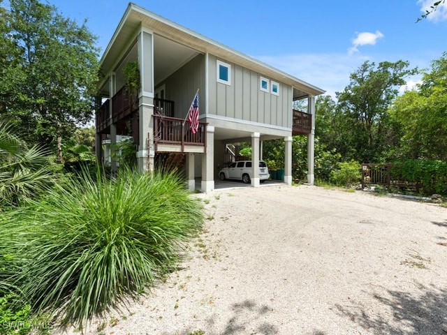 view of front facade with dirt driveway, a carport, board and batten siding, and a balcony