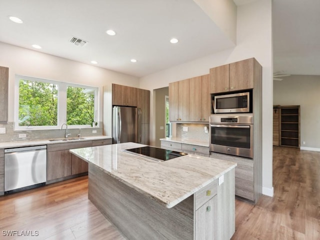 kitchen featuring visible vents, a kitchen island, appliances with stainless steel finishes, light stone counters, and a sink