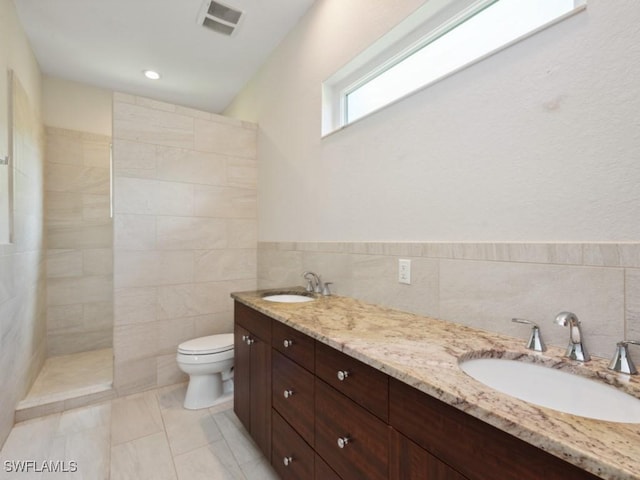 full bathroom with a sink, tile walls, toilet, and double vanity