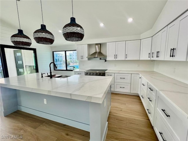 kitchen with stove, a center island with sink, sink, hanging light fixtures, and wall chimney exhaust hood