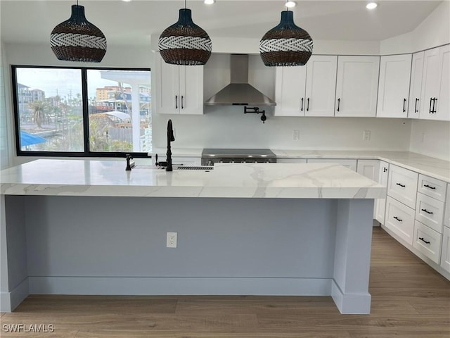 kitchen featuring wall chimney range hood, hanging light fixtures, and an island with sink