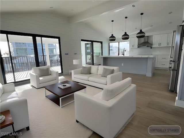 living room with sink, lofted ceiling with beams, and light wood-type flooring