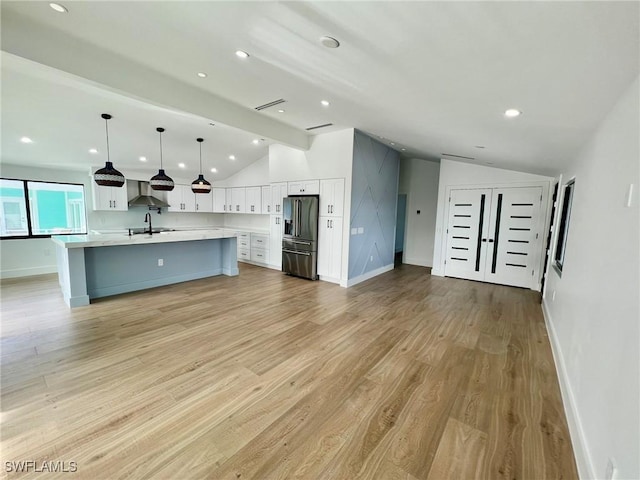 kitchen with stainless steel refrigerator with ice dispenser, pendant lighting, lofted ceiling with beams, white cabinets, and an island with sink