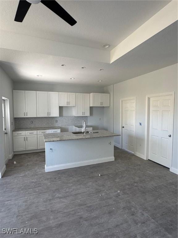 kitchen featuring backsplash, white cabinetry, an island with sink, and ceiling fan