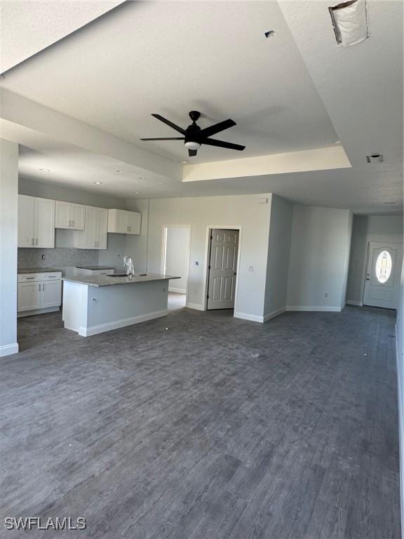 unfurnished living room with dark hardwood / wood-style floors, a raised ceiling, ceiling fan, and sink