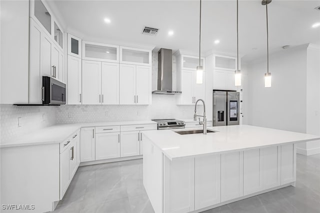 kitchen featuring wall chimney range hood, backsplash, a kitchen island with sink, sink, and stainless steel appliances