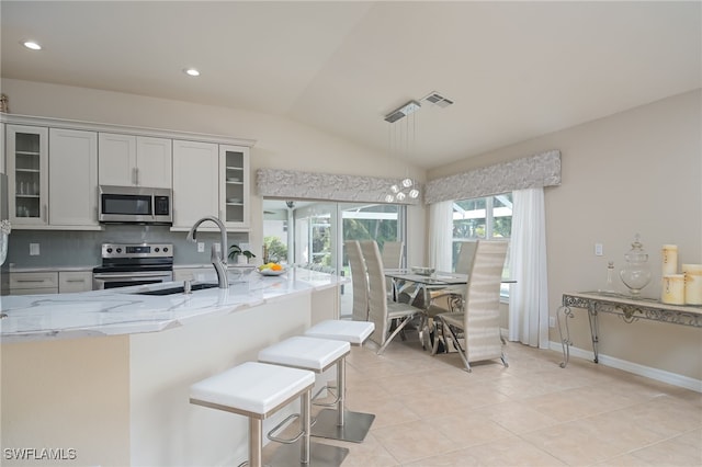 kitchen with glass insert cabinets, a kitchen breakfast bar, light stone countertops, stainless steel appliances, and white cabinetry