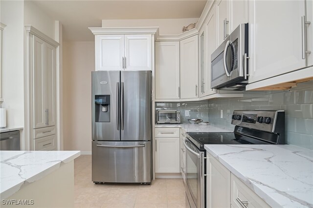 kitchen featuring backsplash, white cabinetry, light stone countertops, light tile patterned floors, and stainless steel appliances