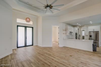 unfurnished living room featuring french doors, a tray ceiling, light hardwood / wood-style floors, and ceiling fan