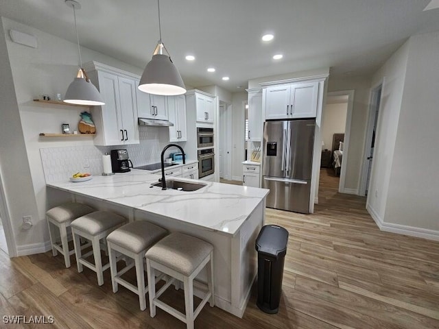 kitchen featuring appliances with stainless steel finishes, light hardwood / wood-style floors, white cabinets, kitchen peninsula, and pendant lighting