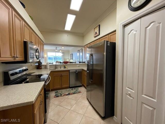 kitchen featuring light tile patterned floors, brown cabinetry, stainless steel appliances, crown molding, and light countertops