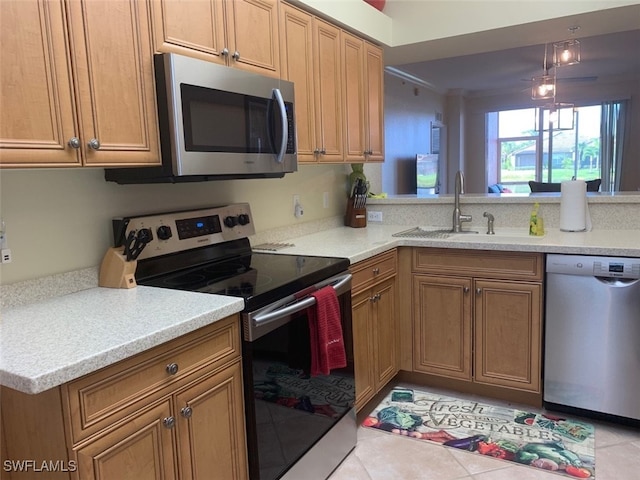 kitchen with light tile patterned floors, appliances with stainless steel finishes, brown cabinets, a peninsula, and a sink