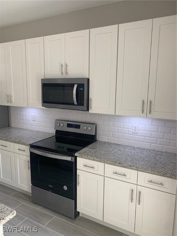 kitchen with backsplash, stainless steel appliances, white cabinets, and light stone countertops