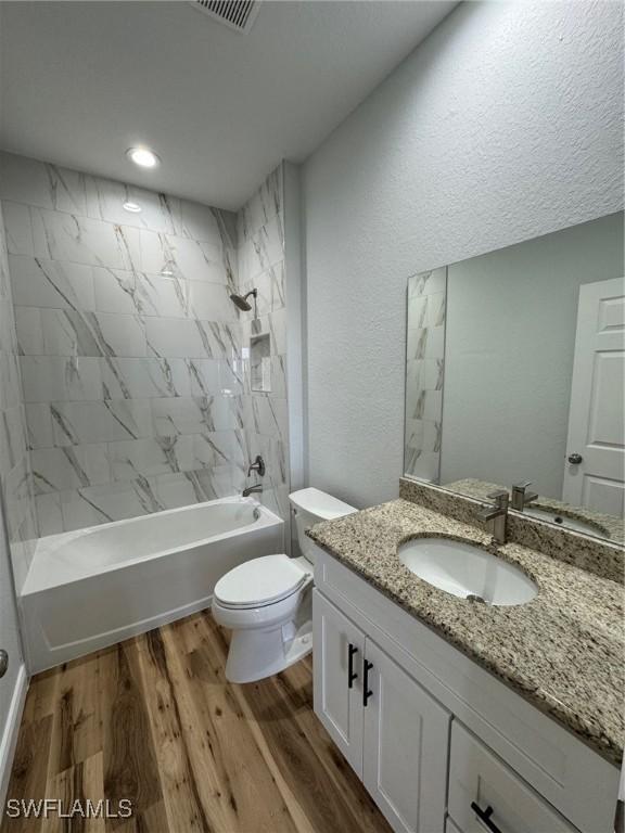 bathroom featuring visible vents, toilet, wood finished floors, vanity, and bathtub / shower combination