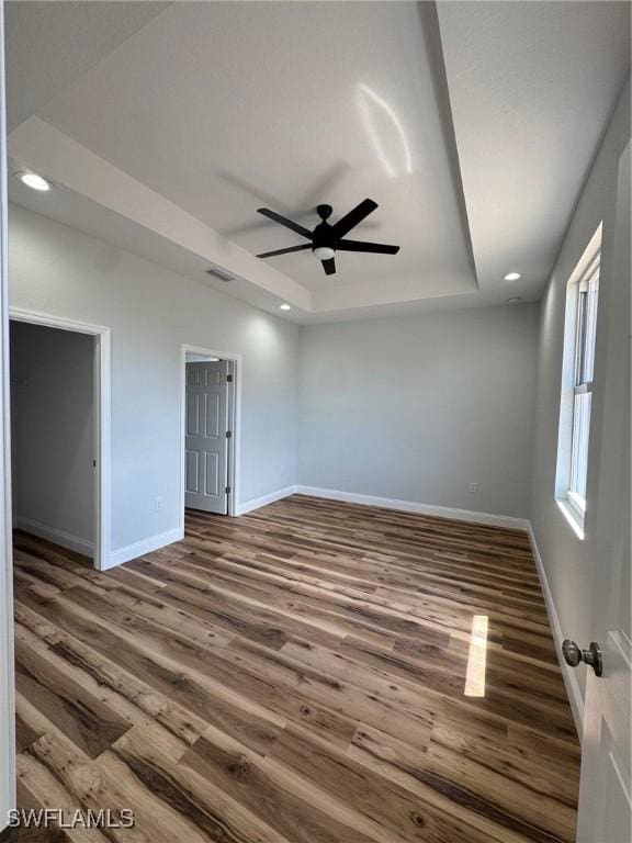 unfurnished room with wood finished floors, ceiling fan, baseboards, visible vents, and a raised ceiling