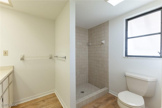 bathroom with hardwood / wood-style floors, vanity, toilet, and tiled shower