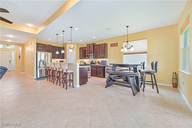 kitchen with appliances with stainless steel finishes, decorative light fixtures, light tile patterned floors, and a breakfast bar area