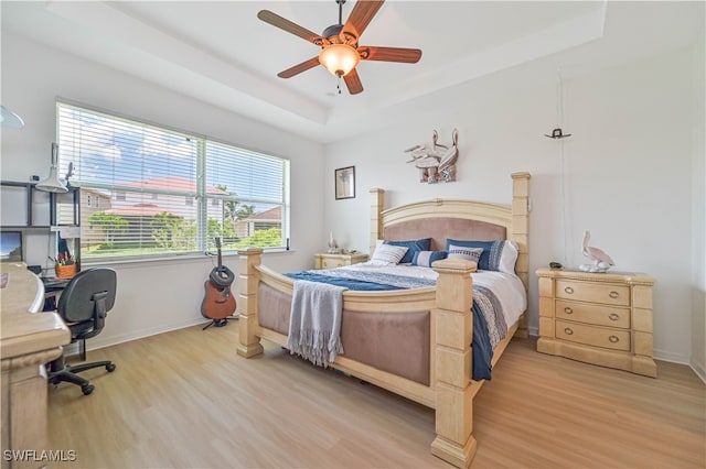 bedroom with light wood-type flooring, ceiling fan, and a tray ceiling