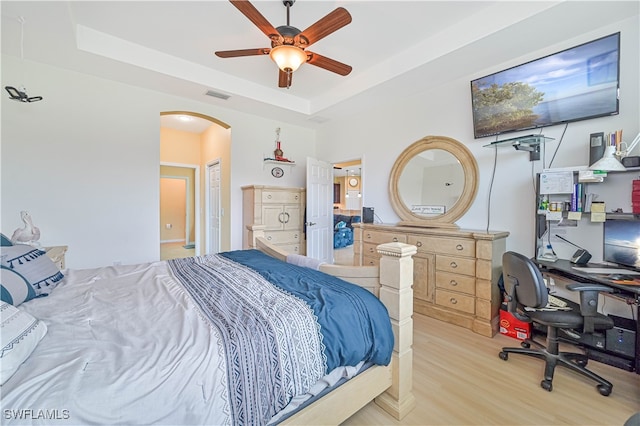 bedroom with ceiling fan, light hardwood / wood-style flooring, and a tray ceiling