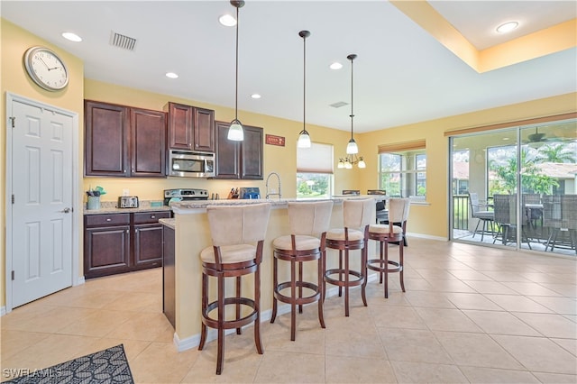 kitchen with stainless steel appliances, pendant lighting, an island with sink, and a kitchen bar