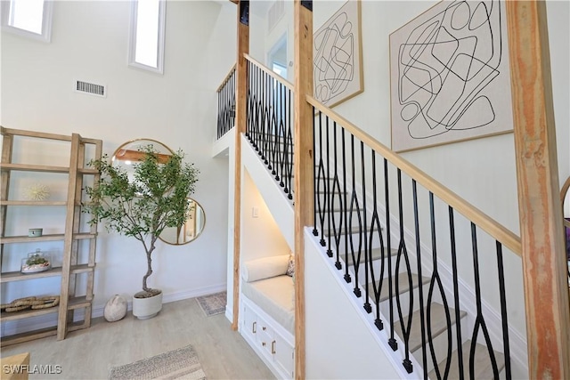 stairway with visible vents, a towering ceiling, baseboards, and wood finished floors