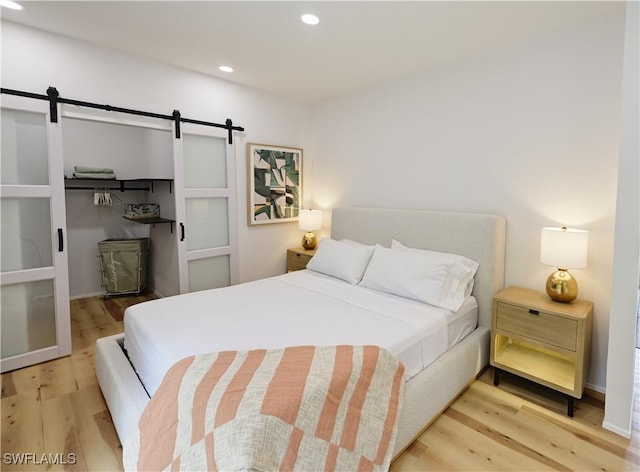 bedroom with light wood-type flooring, a barn door, and recessed lighting