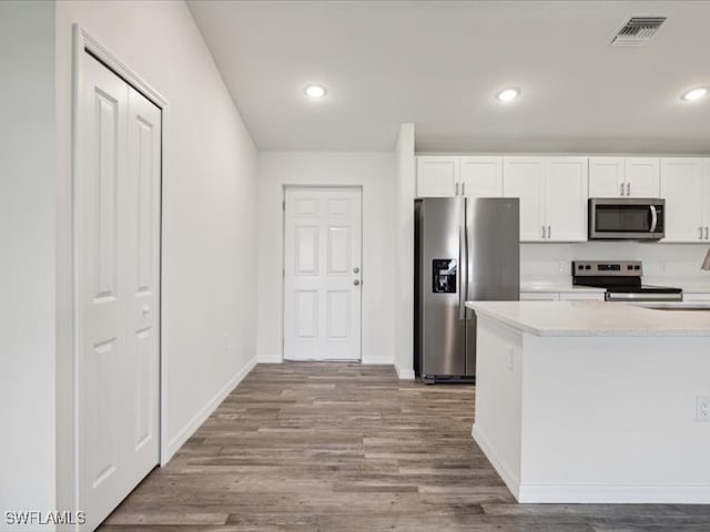 kitchen with stainless steel appliances, light stone countertops, hardwood / wood-style floors, and white cabinetry