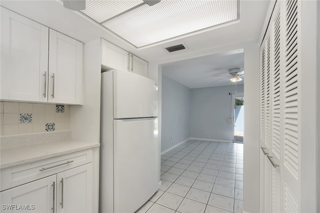 kitchen with white fridge, light tile patterned floors, backsplash, white cabinetry, and ceiling fan