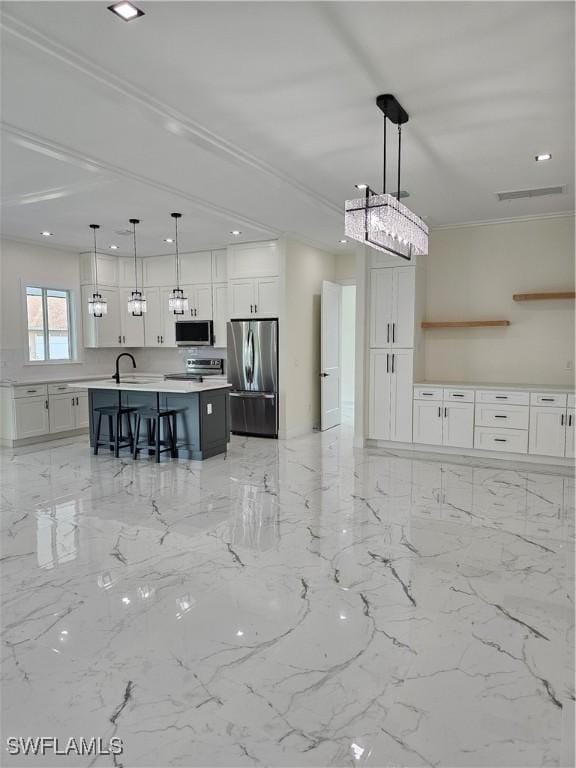 kitchen with sink, hanging light fixtures, stainless steel appliances, an island with sink, and white cabinets