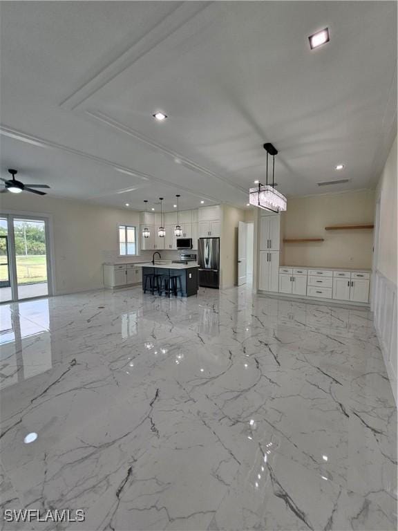 interior space with appliances with stainless steel finishes, a kitchen breakfast bar, a kitchen island with sink, ceiling fan, and decorative light fixtures