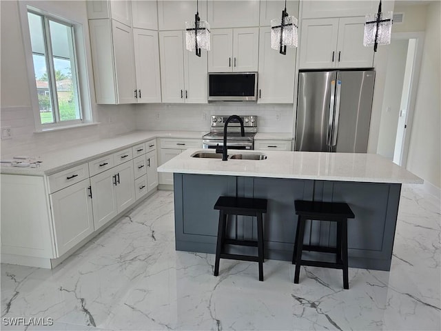 kitchen with white cabinets, hanging light fixtures, a kitchen island with sink, and appliances with stainless steel finishes