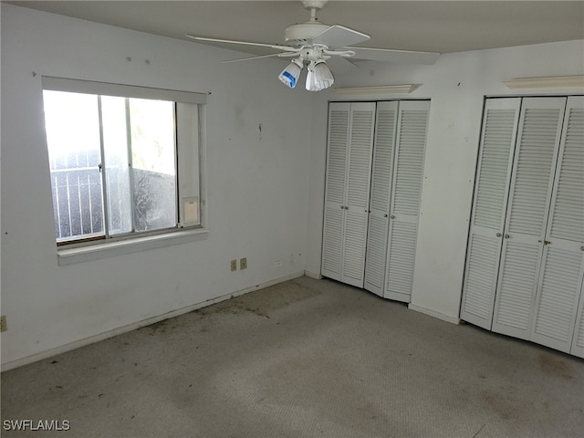 unfurnished bedroom featuring ceiling fan, multiple closets, and light carpet