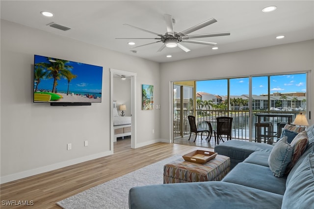 living room with ceiling fan, a water view, and light wood-type flooring