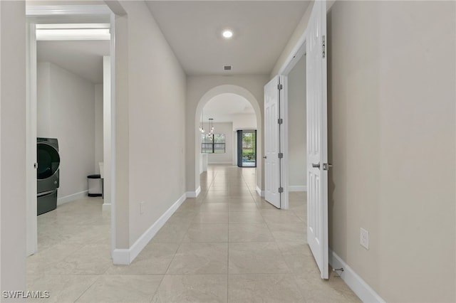 corridor featuring an inviting chandelier, washer / clothes dryer, and light tile patterned floors