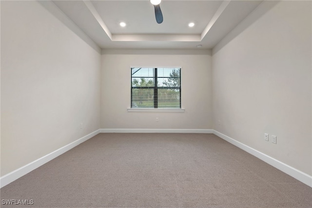 carpeted spare room with ceiling fan and a tray ceiling