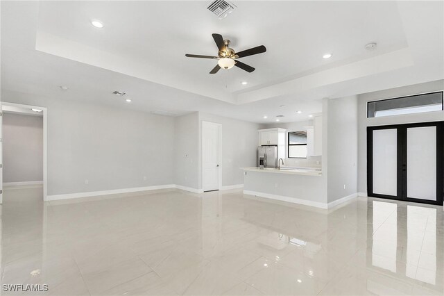 unfurnished living room with ceiling fan, a raised ceiling, sink, and light tile patterned flooring