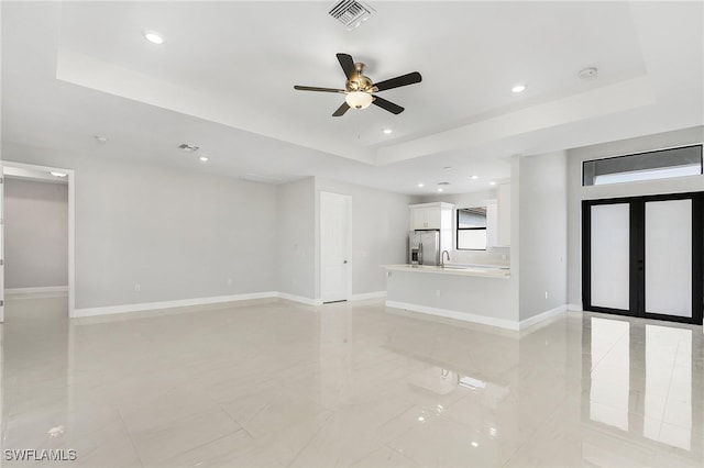 unfurnished living room with a tray ceiling, ceiling fan, and french doors