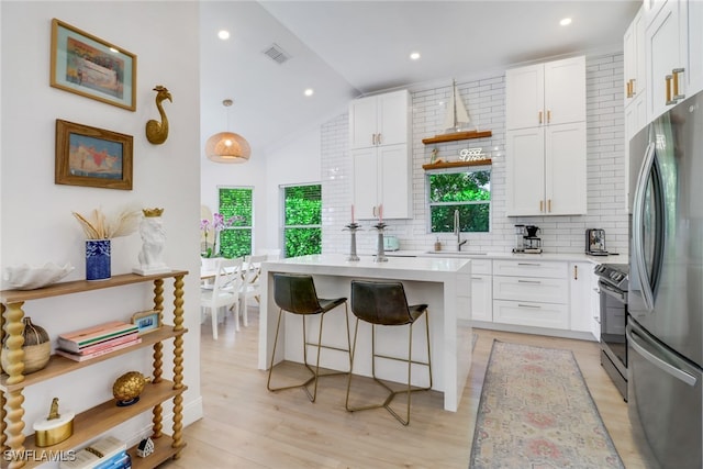 kitchen featuring appliances with stainless steel finishes, vaulted ceiling, decorative backsplash, and white cabinets