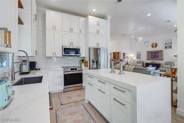 kitchen featuring light wood-type flooring, backsplash, appliances with stainless steel finishes, white cabinetry, and a center island