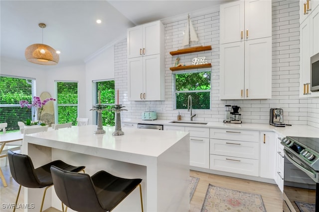 kitchen featuring appliances with stainless steel finishes, light hardwood / wood-style flooring, sink, lofted ceiling, and hanging light fixtures