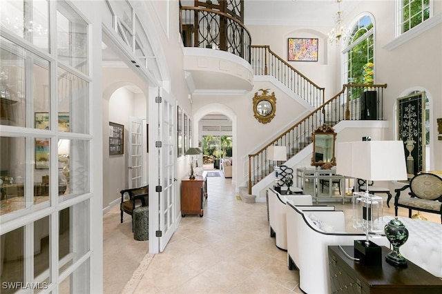 tiled entrance foyer featuring french doors, a towering ceiling, crown molding, and a notable chandelier