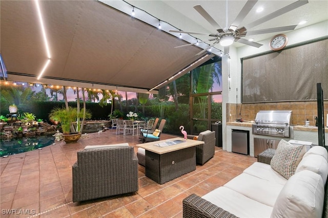 patio terrace at dusk with an outdoor hangout area, an outdoor kitchen, ceiling fan, and a grill