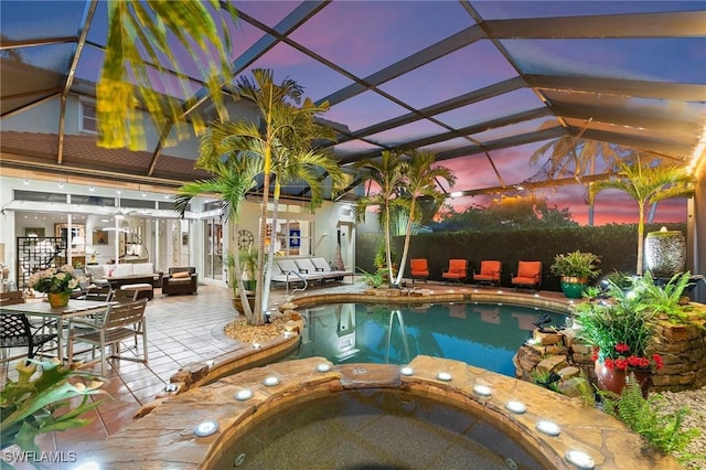 pool at dusk featuring outdoor lounge area, glass enclosure, and a patio area