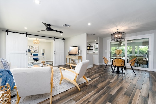 living room featuring a barn door, ceiling fan with notable chandelier, and dark hardwood / wood-style flooring