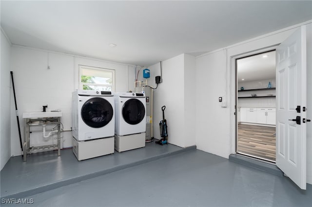 laundry area with electric water heater, washing machine and dryer, and sink