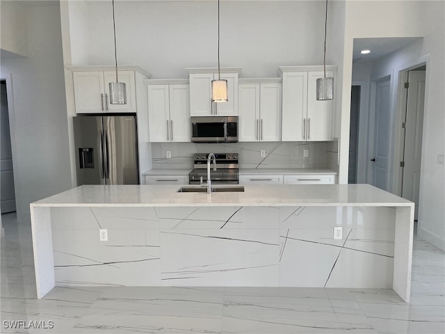 kitchen with white cabinets, appliances with stainless steel finishes, an island with sink, and tasteful backsplash