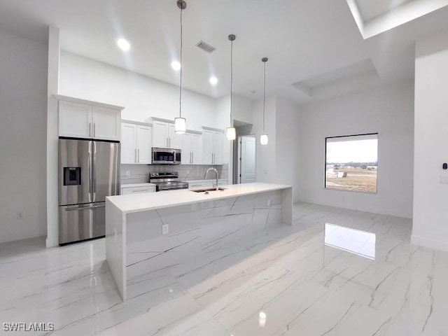 kitchen with pendant lighting, white cabinetry, stainless steel appliances, sink, and a center island with sink