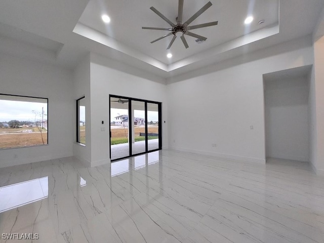 unfurnished room with a tray ceiling, plenty of natural light, and ceiling fan