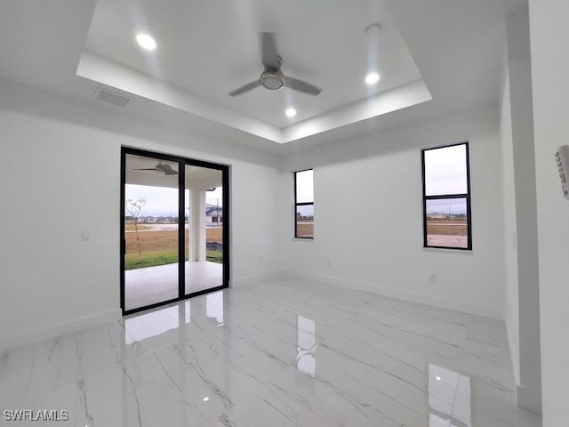 unfurnished room with a tray ceiling, a healthy amount of sunlight, and ceiling fan